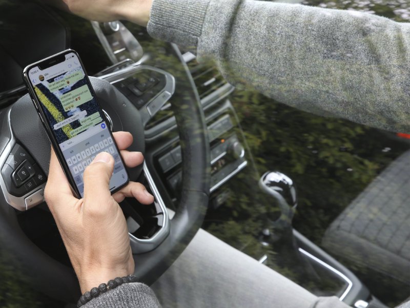 ablenkung-am-steuer-polizeikontrolle-bussgeld-3.jpg Hand tippt eine Nachricht auf dem Smartphone direkt hinter dem Lenkrad im Auto.